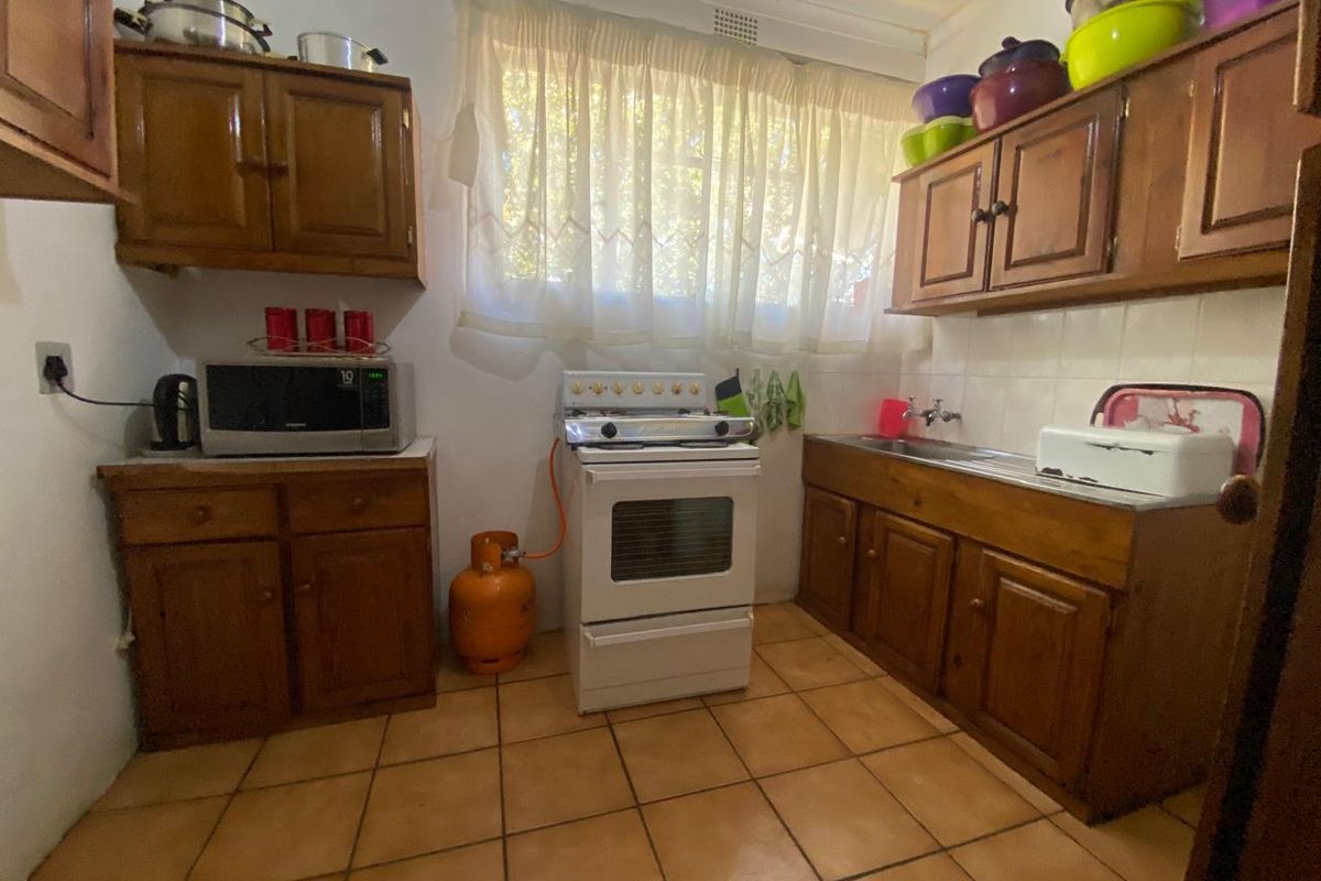 A functional kitchen featuring wooden cabinetry, a gas stove, and tiled flooring, offering a dated aesthetic with potential for modern renovation.