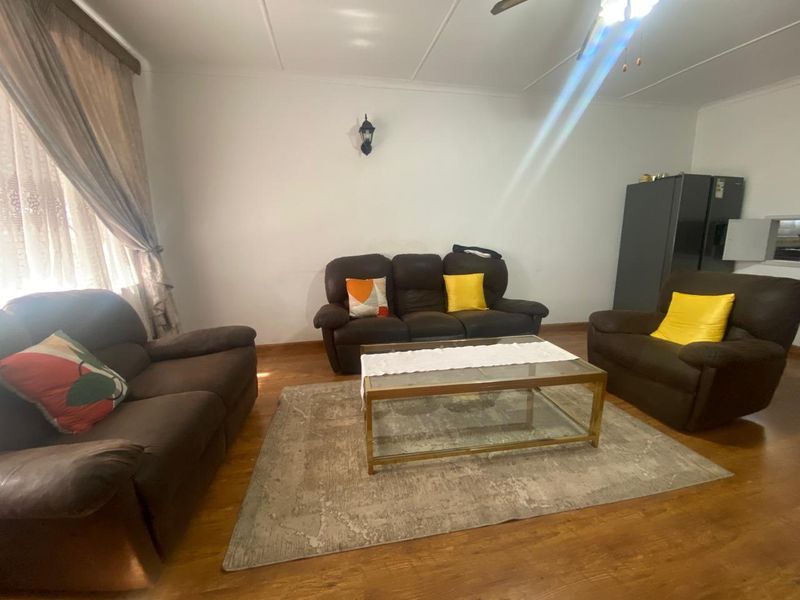 A spacious living room featuring laminate flooring, a ceiling fan, and a wall-mounted light fixture, offering a comfortable and functional living space.