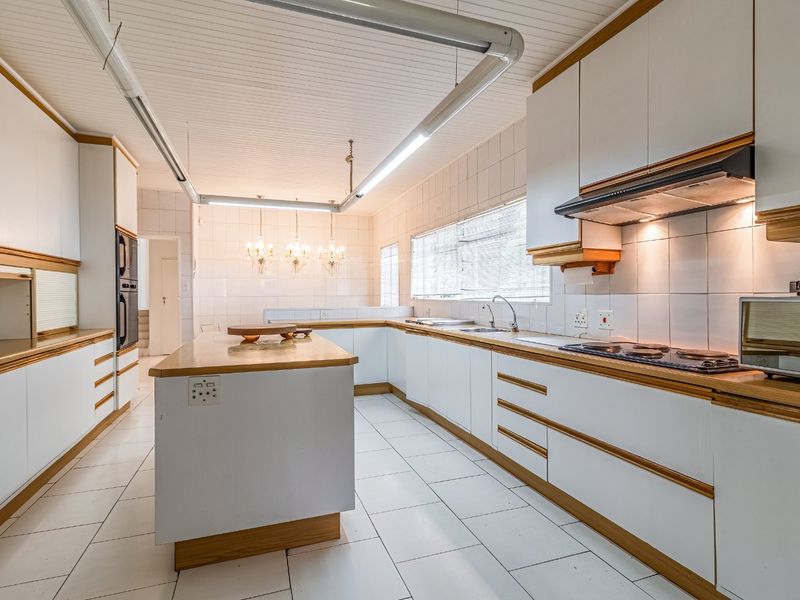 Spacious kitchen featuring white cabinetry with wood trim, a central island, built-in double oven, cooktop, and tiled flooring throughout.