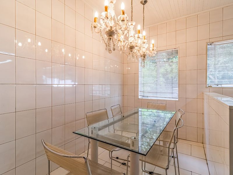 A dining area featuring fully tiled walls and floors, a beadboard ceiling, and natural light through venetian blinds.