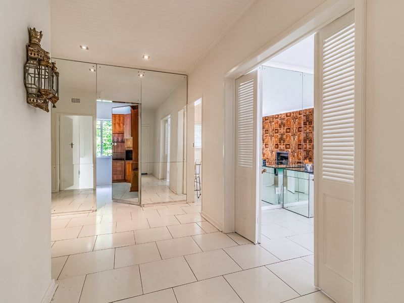 Bright and spacious hallway featuring white tiled flooring, mirrored wall panels, and louvered doors leading to adjacent rooms.