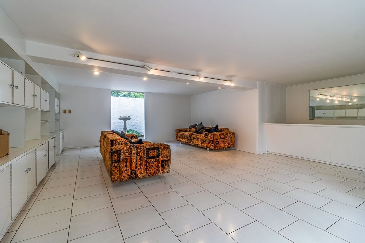 Spacious living area featuring white tiled flooring, extensive built-in cabinetry, and track lighting, offering a bright and versatile space.