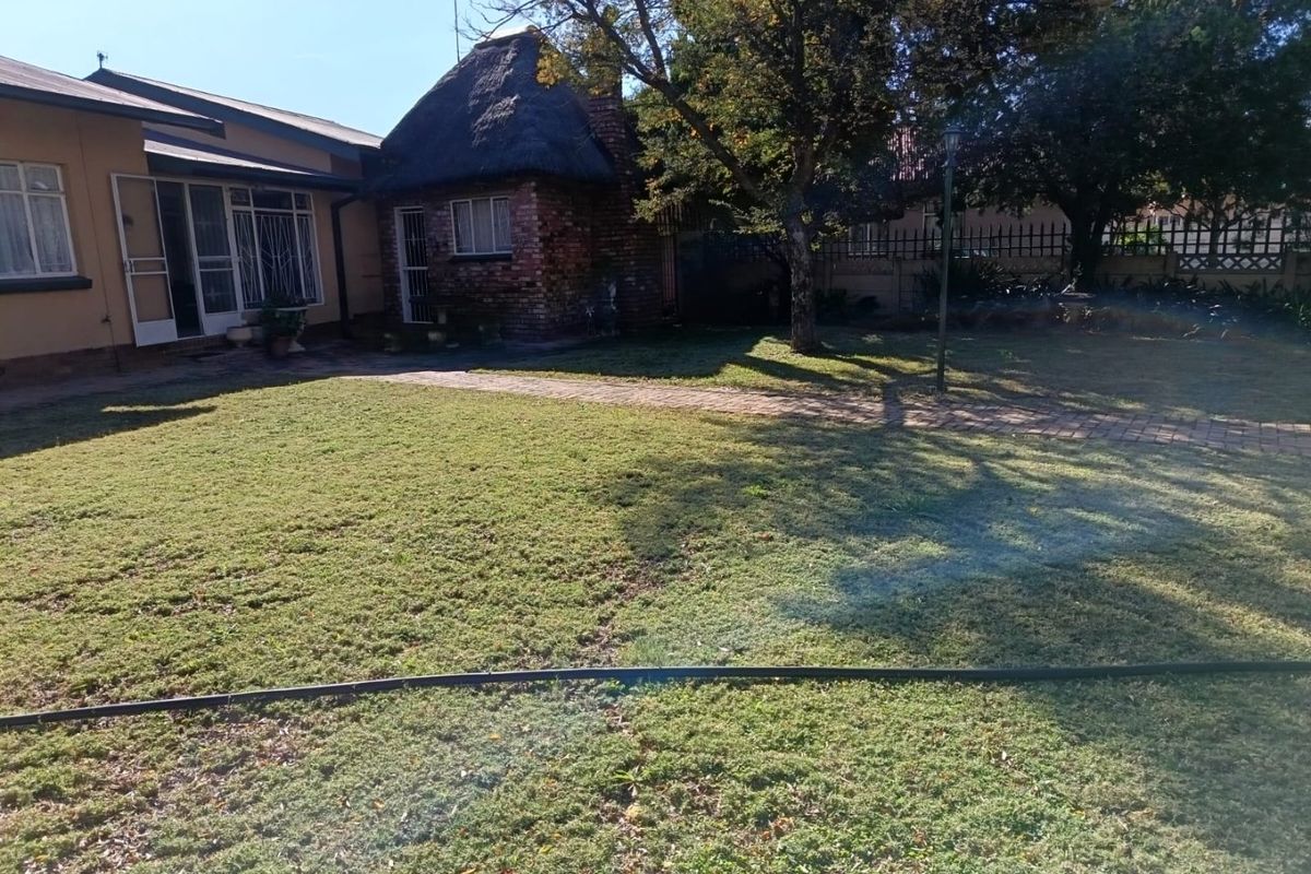 A rear garden view featuring a lawn, paved pathway, and a brick structure with a traditional thatched roof.