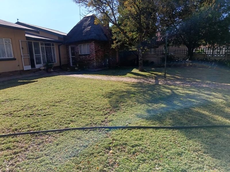 A rear garden view featuring a lawn, paved pathway, and a brick structure with a traditional thatched roof.