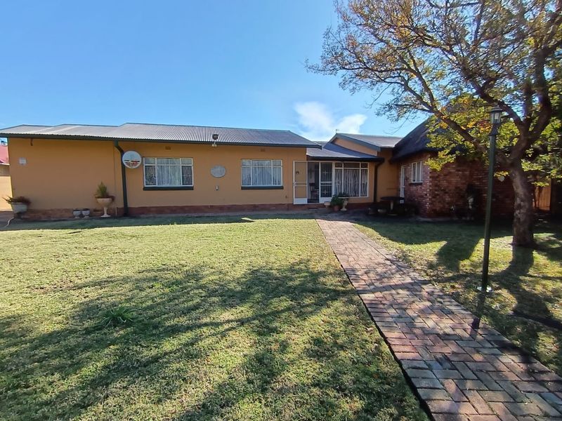 A view of the rear exterior of the house featuring a brick paved walkway leading to the entrance and a well-maintained lawn.