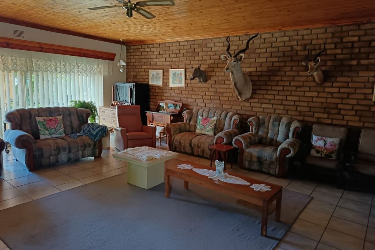 Spacious living room featuring an exposed brick feature wall, timber ceiling, and tiled flooring, offering a traditional aesthetic with potential for modern updates.