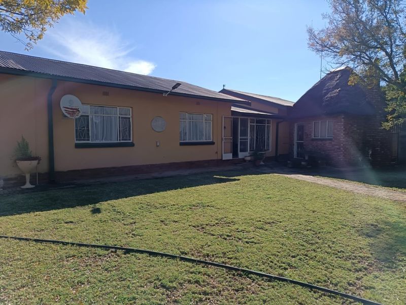 Rear view of the property featuring a lawn, brick pathway, and a combination of plastered and thatched roof structures.