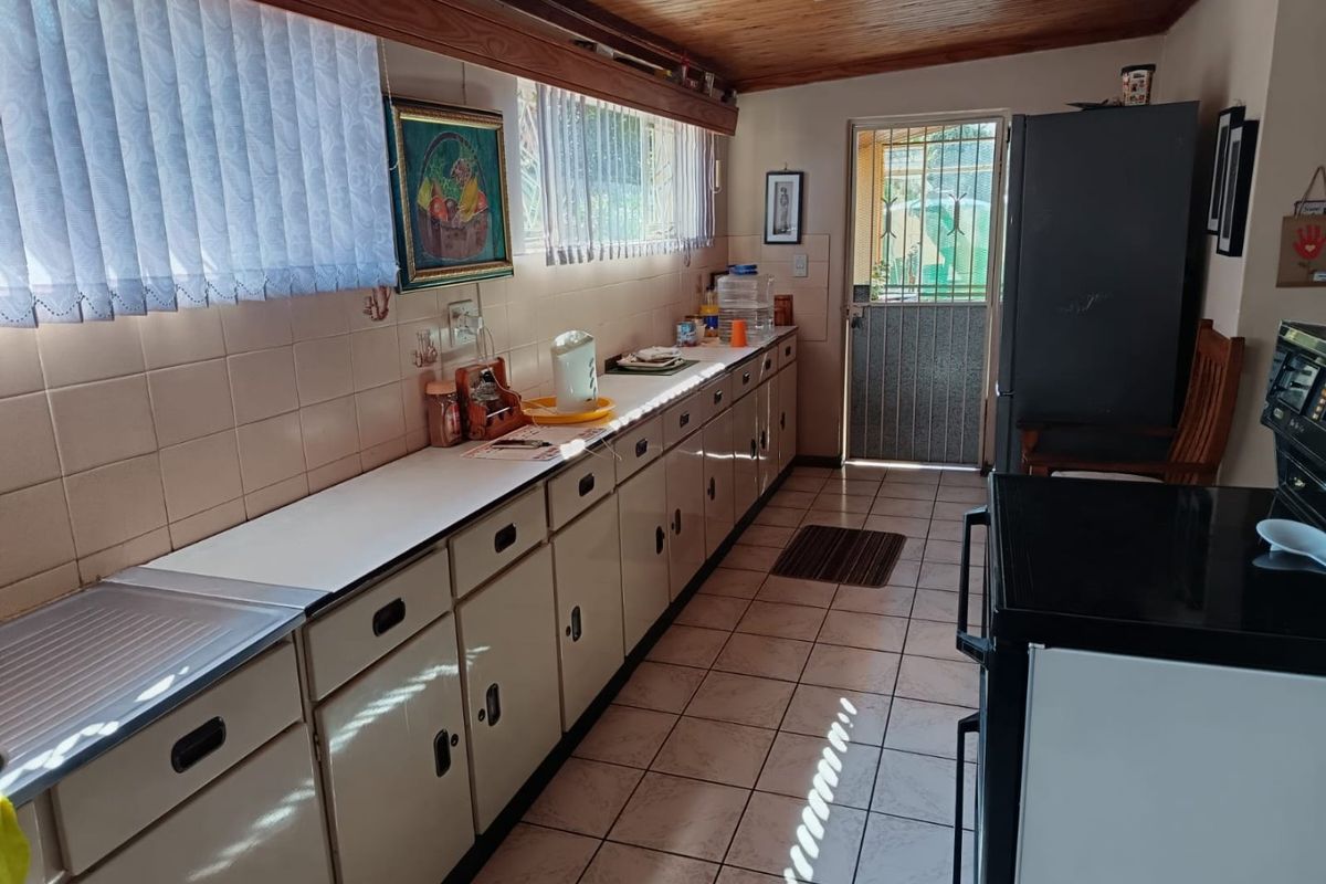 A functional kitchen featuring extensive laminate cabinetry, tiled splashbacks, and a timber-paneled ceiling, with direct access to the exterior via a security gate.