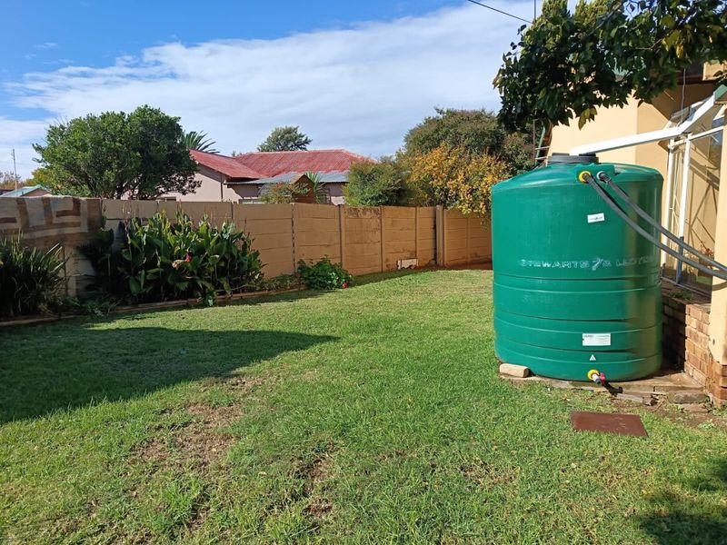 A private rear garden featuring a green water storage tank connected to the house gutter system and a precast concrete boundary wall.
