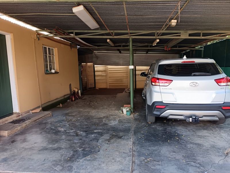 A covered carport or garage area featuring a corrugated metal roof, concrete flooring, and steel support columns.