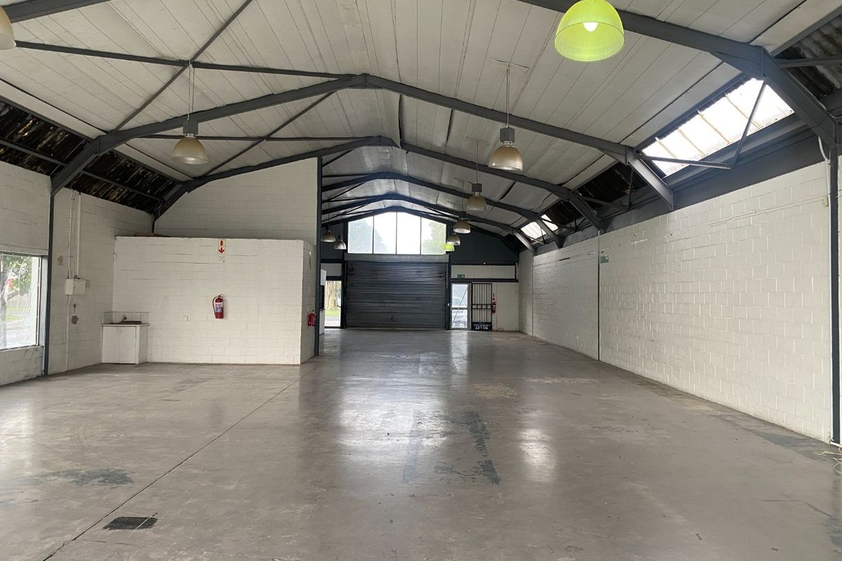 Spacious open-plan commercial warehouse featuring high ceilings with exposed steel trusses, polished concrete floors, and large roller shutter access.
