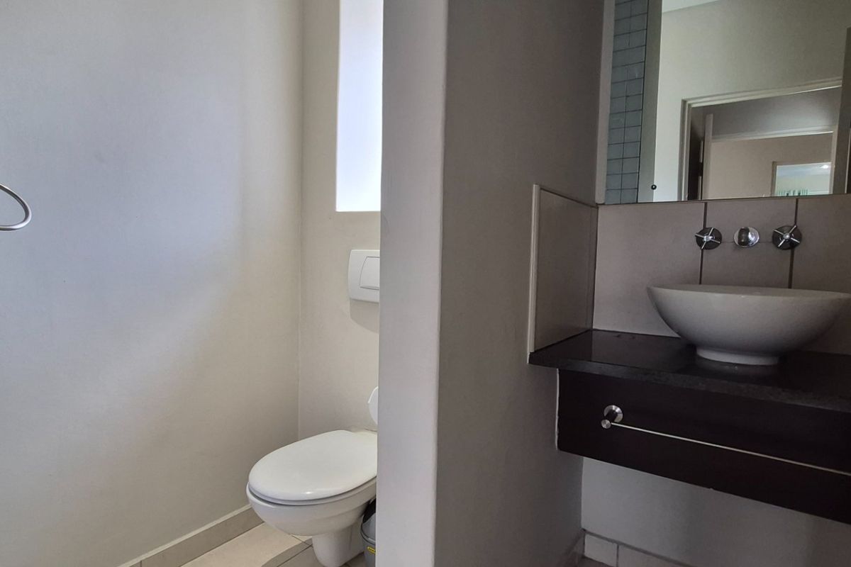 A functional bathroom featuring a wall-mounted toilet, a modern vessel sink set on a vanity cabinet, and wall-mounted fixtures.