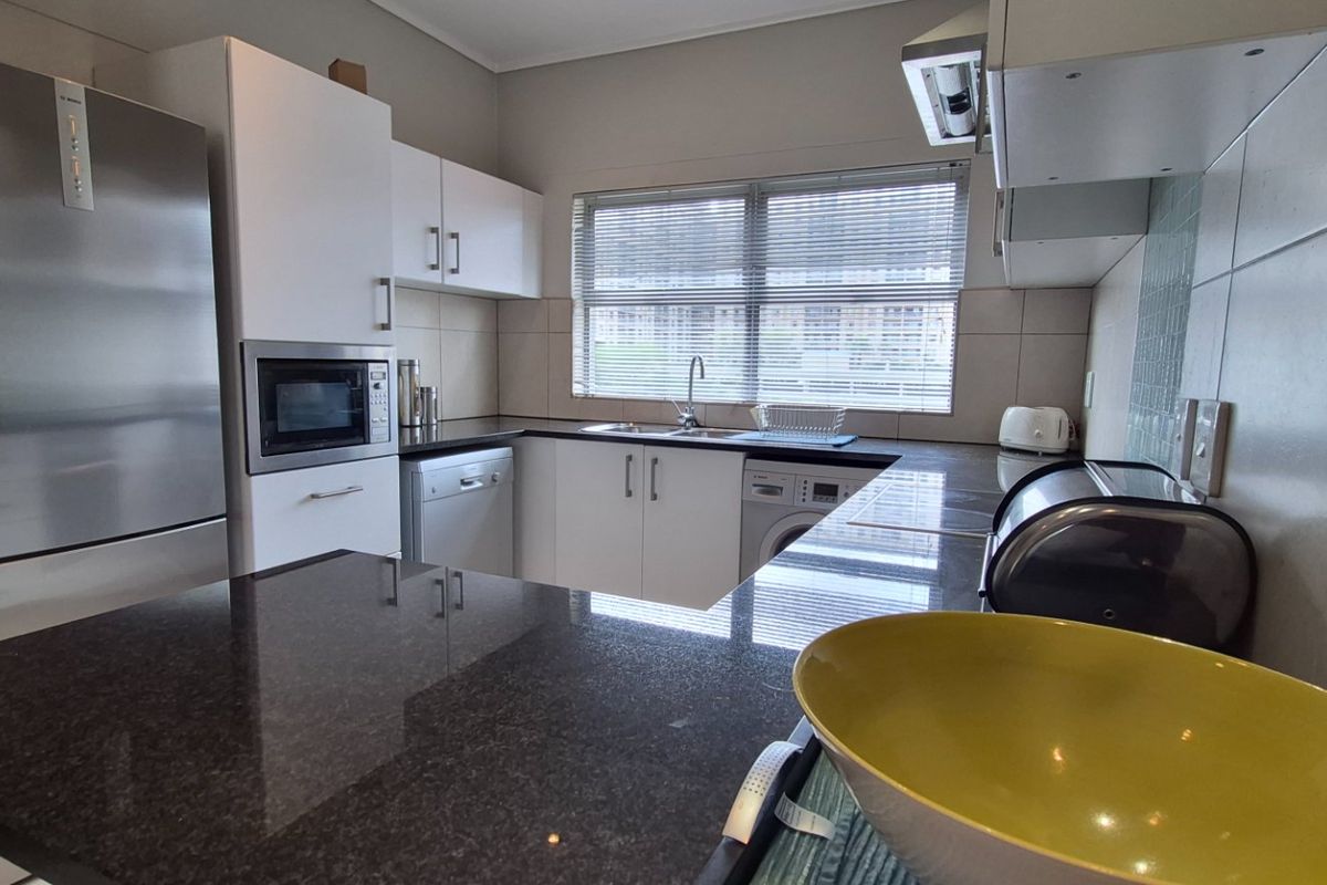A functional kitchen featuring granite countertops, ample built-in cabinetry, a stainless steel sink, and integrated appliances including a microwave and extractor fan.