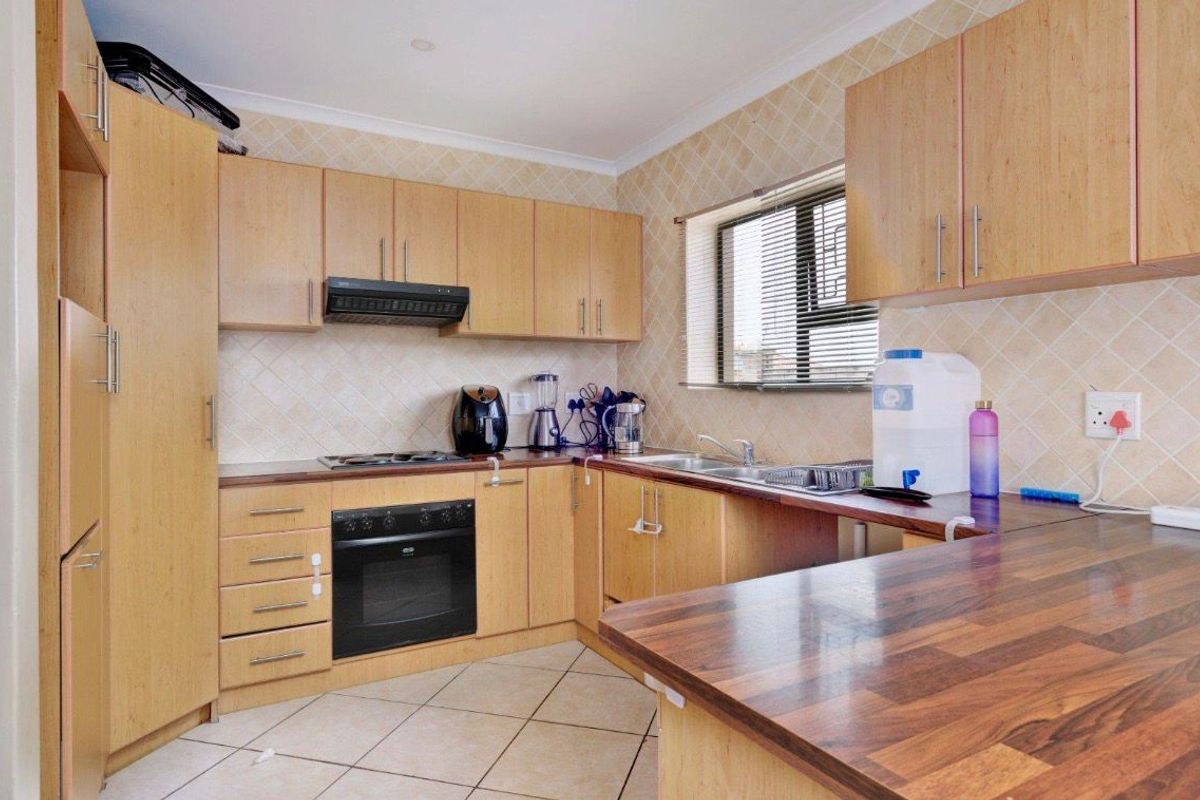 A functional kitchen featuring light wood-finish cabinetry, dark laminate countertops, a built-in oven with hob, and tiled backsplash and flooring.