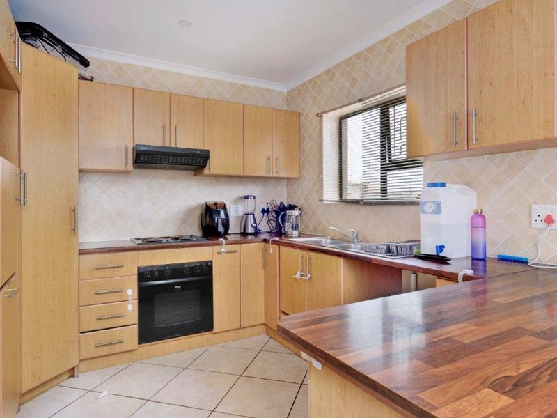 A functional kitchen featuring light wood-finish cabinetry, dark laminate countertops, a built-in oven with hob, and tiled backsplash and flooring.