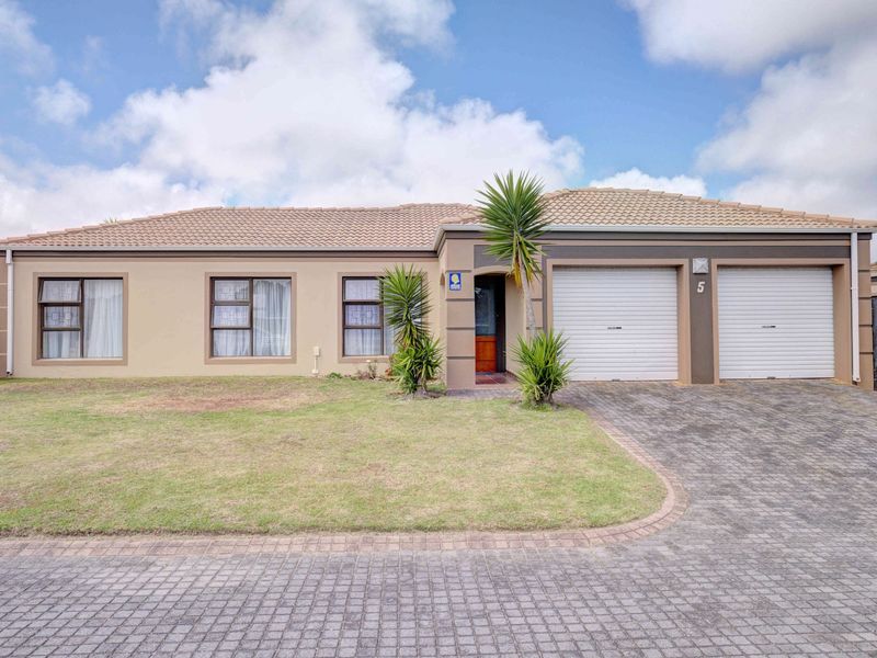 Front elevation of a well-maintained townhouse featuring a double garage, paved driveway, and neat front lawn with established landscaping.