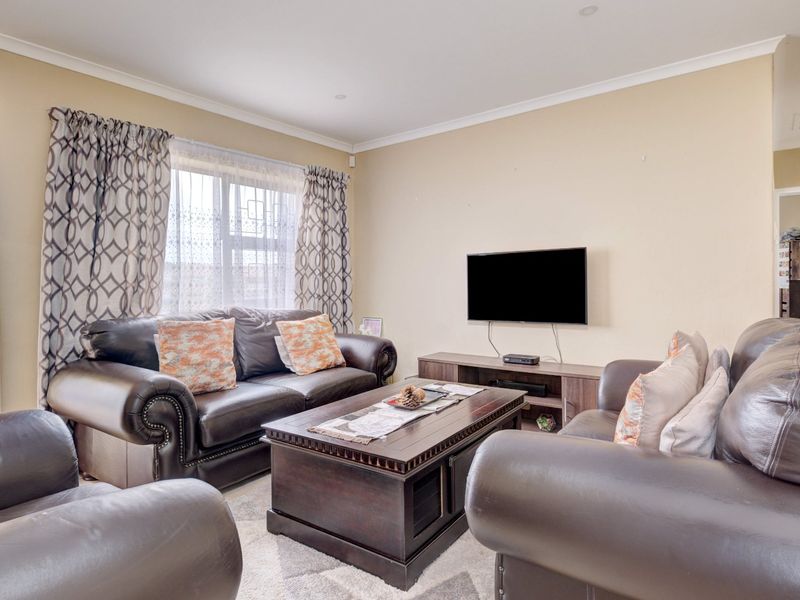 A comfortable living room featuring neutral wall tones, recessed downlighting, and a large window with curtain treatments, providing a functional and inviting space.