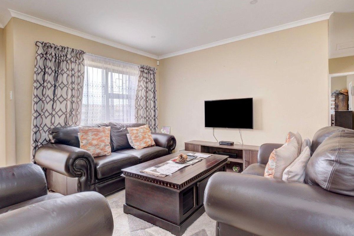 A comfortable living room featuring neutral wall tones, cove cornicing, and a window fitted with security bars.