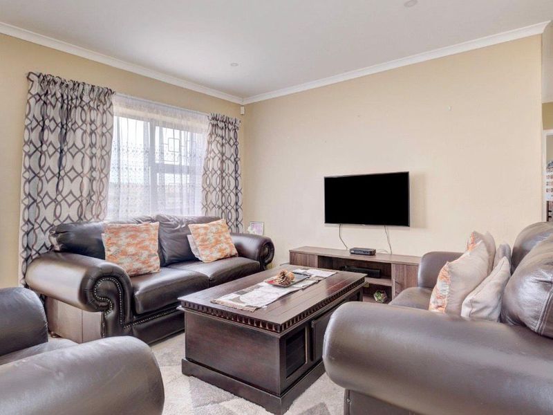 A comfortable living room featuring neutral wall tones, cove cornicing, and a window fitted with security bars.