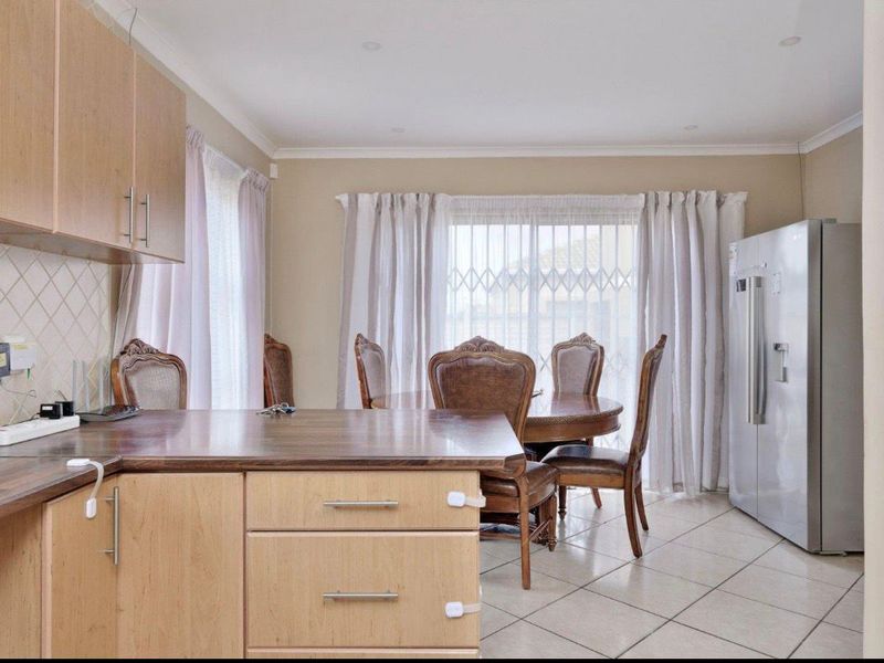 Open-plan kitchen and dining area featuring light wood cabinetry, laminate countertops, tiled flooring, and direct access to the exterior through a sliding glass door.