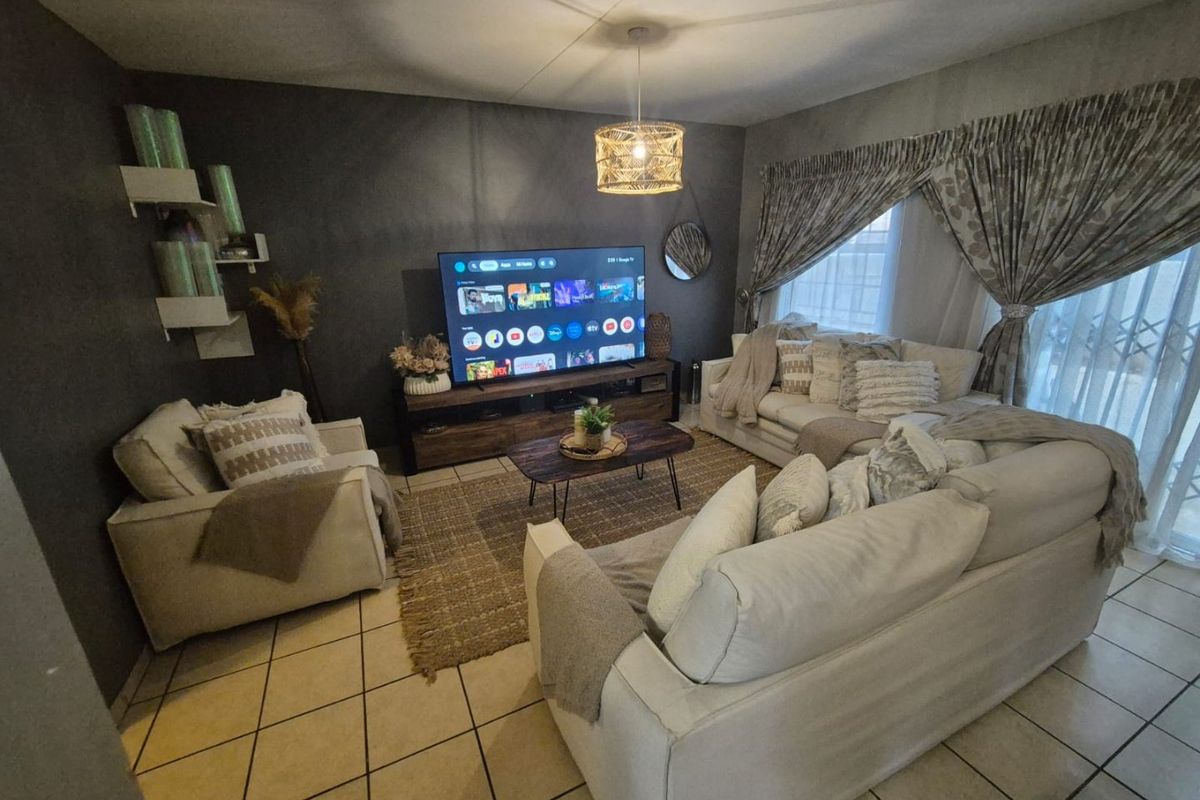 A cozy living room featuring tiled flooring, a dark accent wall, and natural light filtered through curtains.