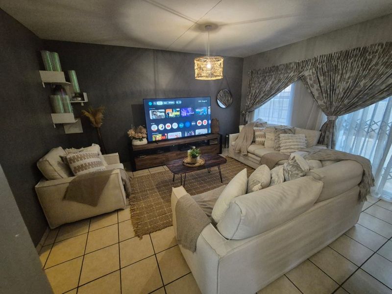 A cozy living room featuring tiled flooring, a dark accent wall, and natural light filtered through curtains.