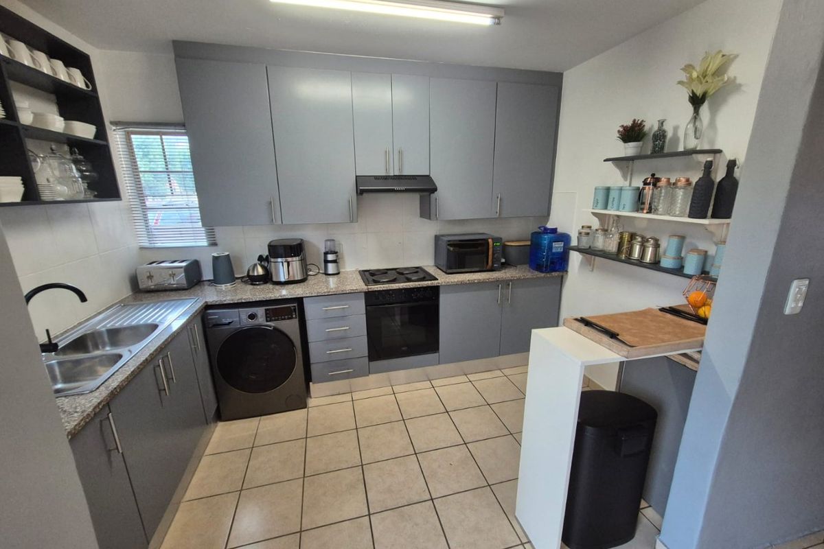 A functional kitchen featuring grey built-in cabinetry, granite countertops, a built-in oven with hob, and tiled flooring.