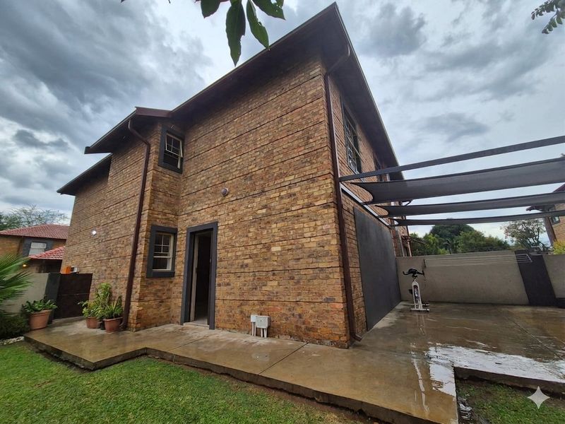 Rear view of the townhouse featuring a face brick facade, a concrete patio area with a shade sail, and access to the garden.