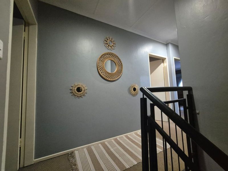 A well-maintained hallway featuring a metal staircase railing and neutral carpeted flooring, leading to multiple interior doorways.