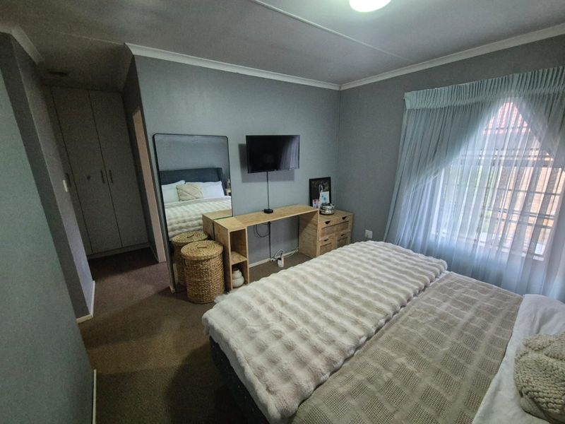 A functional bedroom featuring built-in cupboards, carpeted flooring, and a window with curtain rails, offering a comfortable and practical living space.