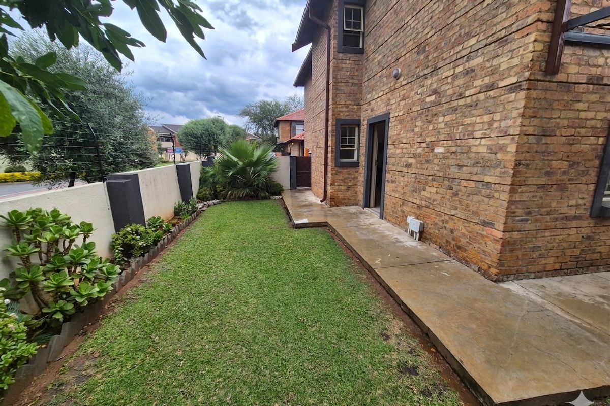 A private rear garden area featuring a well-maintained lawn, concrete pathway, and secure perimeter wall with electric fencing.