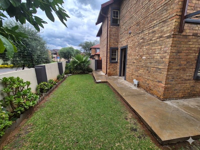 A private rear garden area featuring a well-maintained lawn, concrete pathway, and secure perimeter wall with electric fencing.