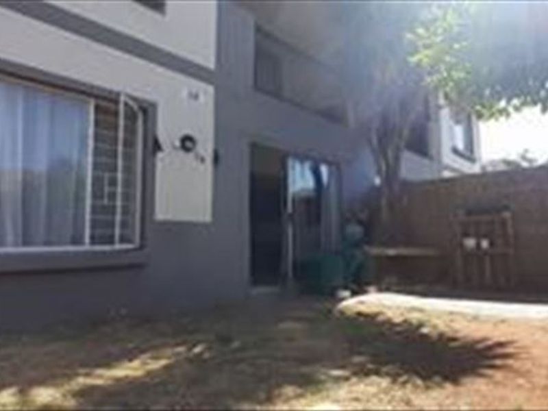 Rear view of the townhouse featuring a small garden area, paved section, and sliding door access to the interior living space.
