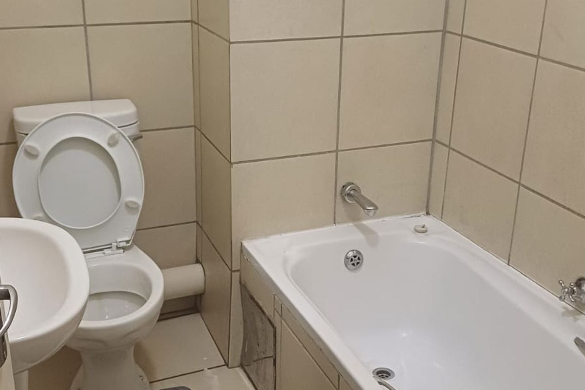 A functional bathroom featuring a pedestal basin, toilet, and bathtub with tiled walls and flooring, requiring minor maintenance to the bathtub apron.