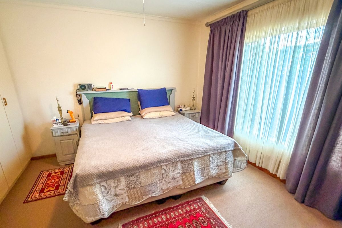 A bedroom featuring built-in wardrobes and a large window with curtain treatments, providing natural light and storage space.