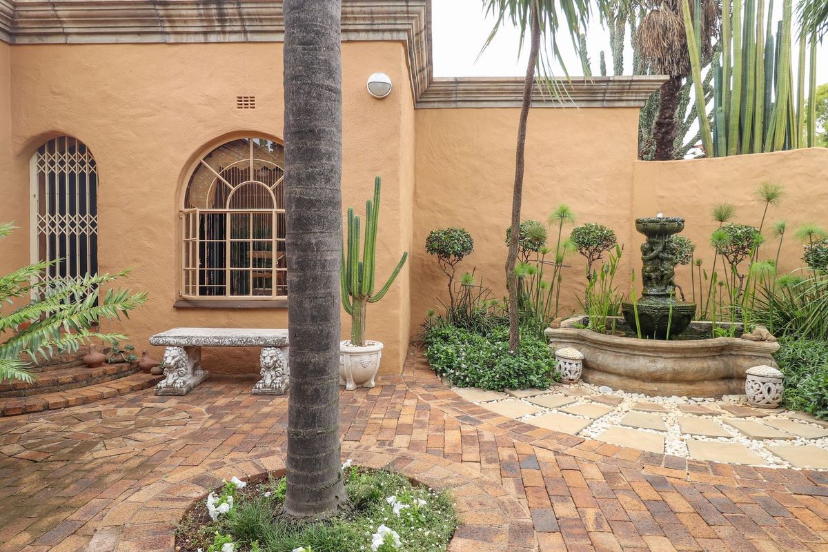 A landscaped rear courtyard featuring brick paving, a decorative stone fountain, and an arched window with security gate.