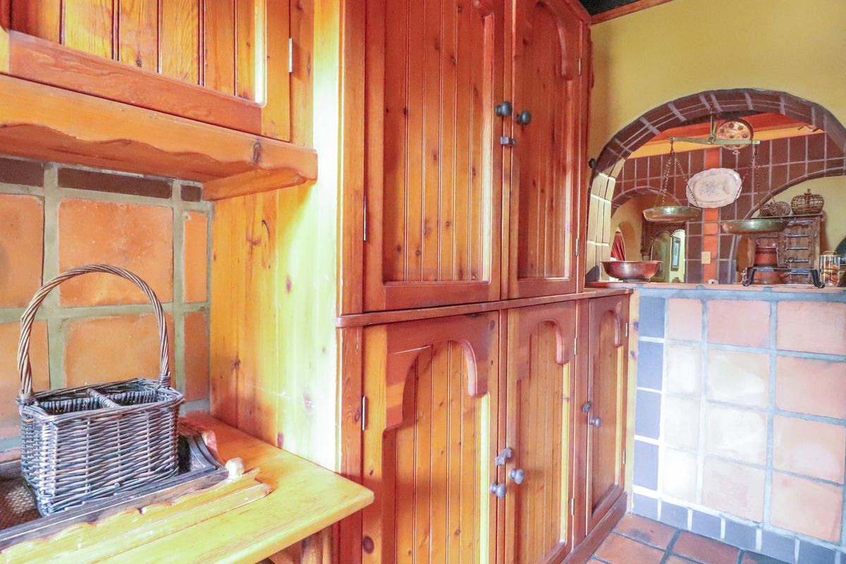 A rustic kitchen featuring traditional timber cabinetry, terracotta tile splashbacks, and a distinctive brick archway connecting to an adjacent space.