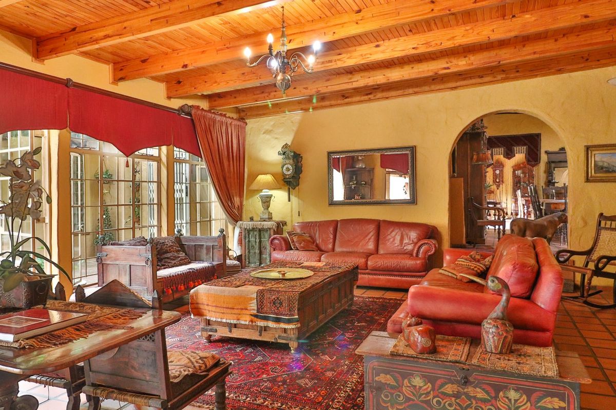 Spacious living room featuring a warm, rustic aesthetic with exposed timber beam ceilings, terracotta floor tiles, and an elegant arched entryway.