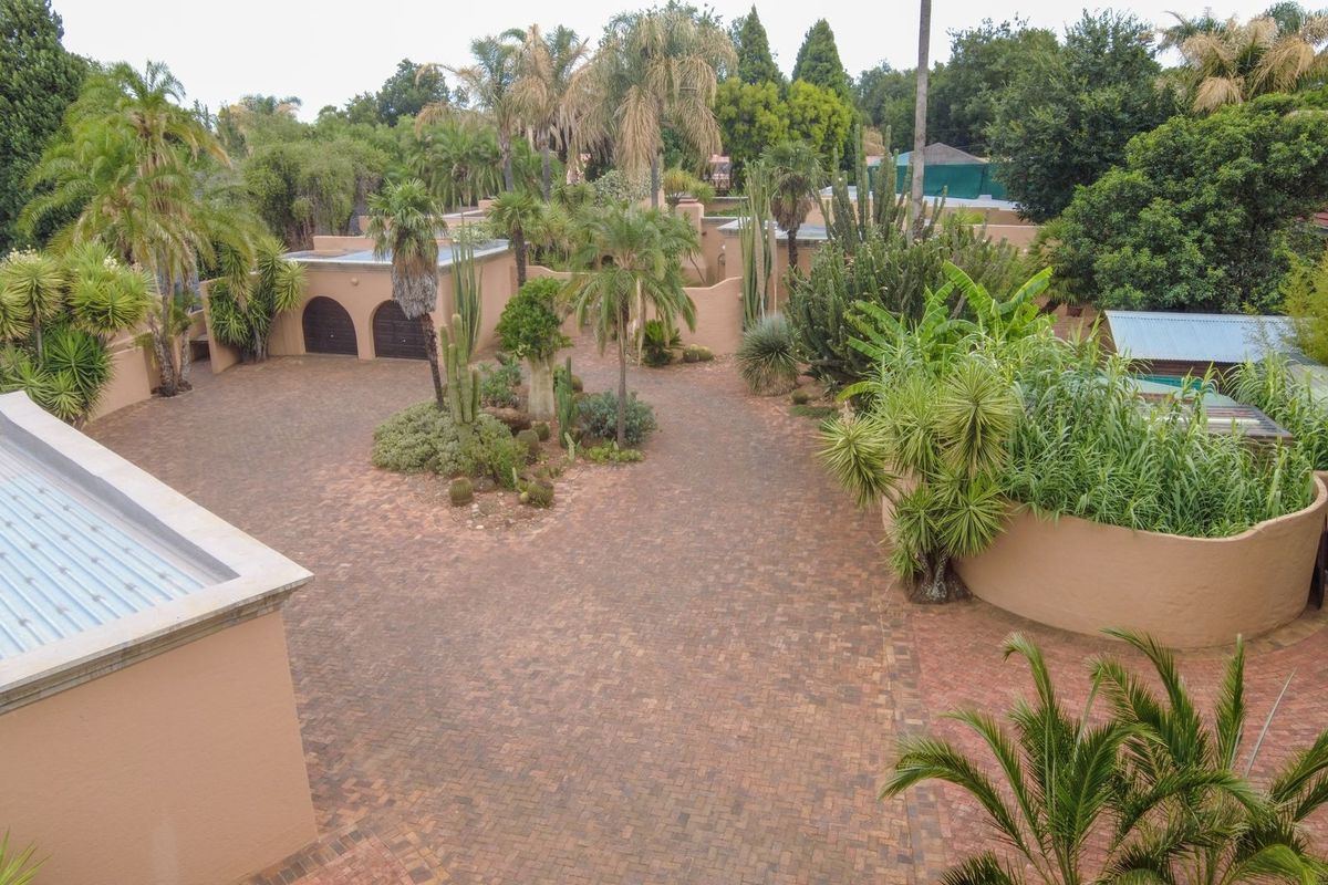 Aerial view of a spacious property featuring a large brick-paved driveway, established landscaped gardens, and secure boundary walls.