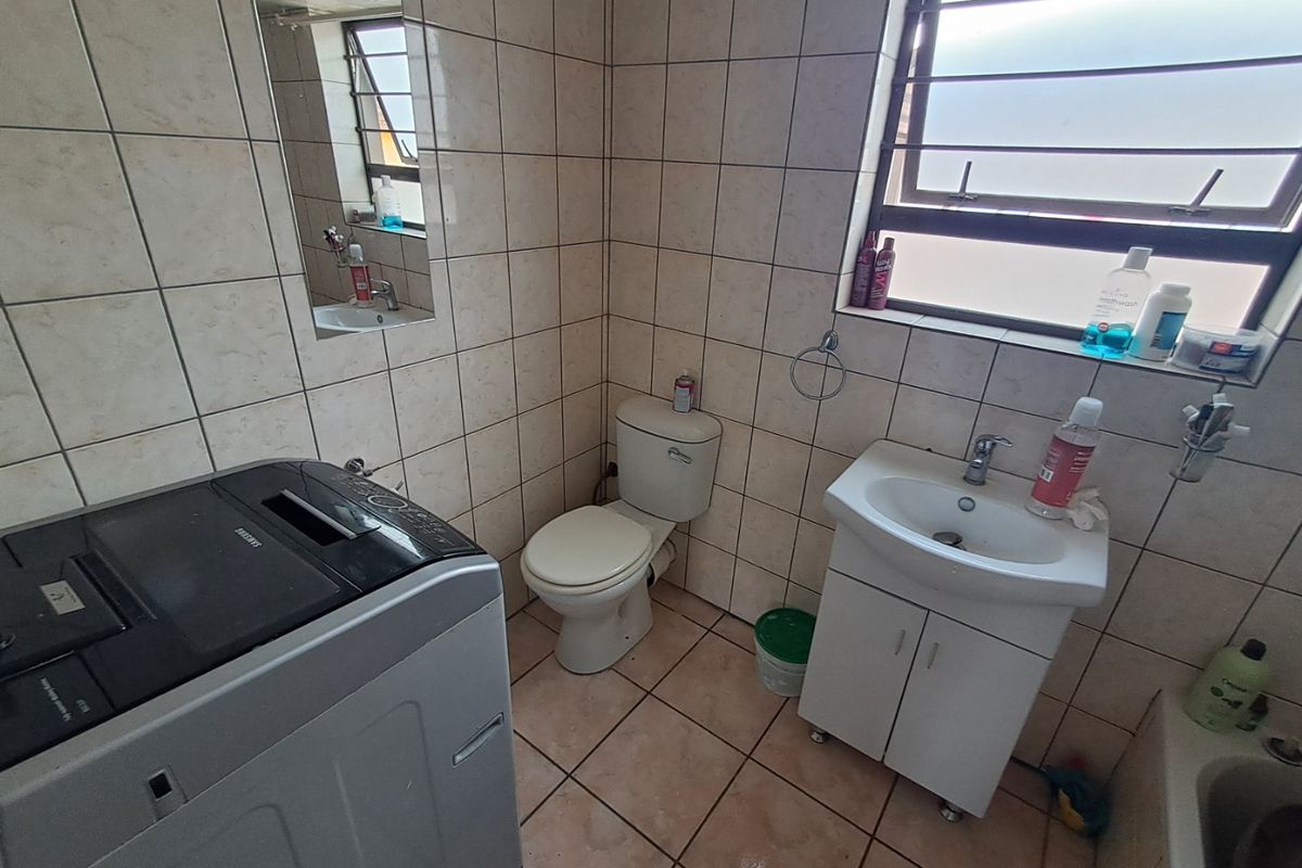 A functional bathroom featuring ceramic tiling, a vanity basin, and a toilet, with a louvre window providing natural light.