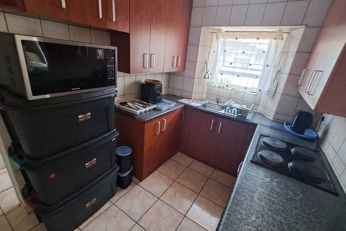 Compact kitchen featuring laminate cabinetry, granite countertops, an electric hob, and tiled finishes, offering a functional layout with potential for modern updates.