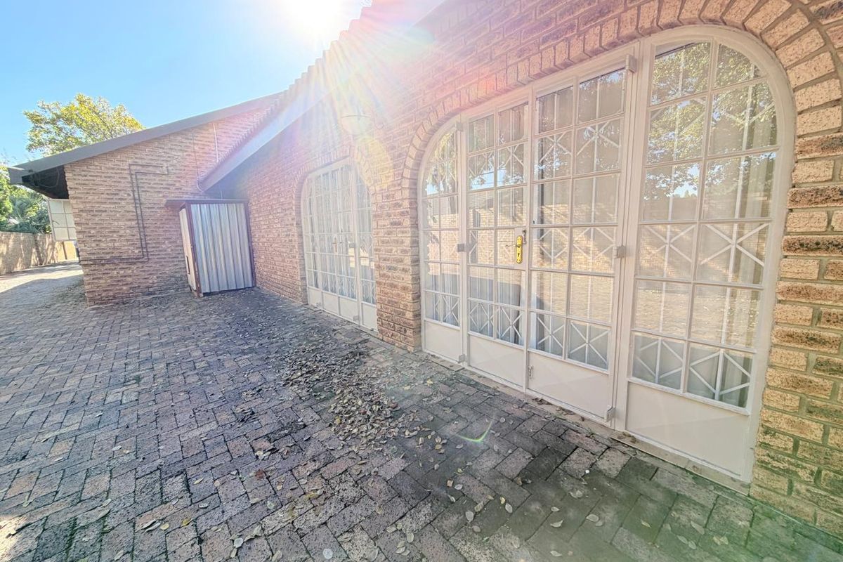 Rear exterior view featuring a paved patio area, brick facade, and large metal-framed glass doors with security bars.
