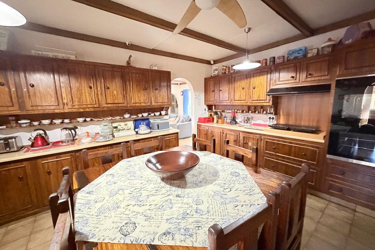 Spacious kitchen featuring extensive wooden cabinetry, built-in oven, hob, and exposed ceiling beams, offering a traditional aesthetic with functional layout.