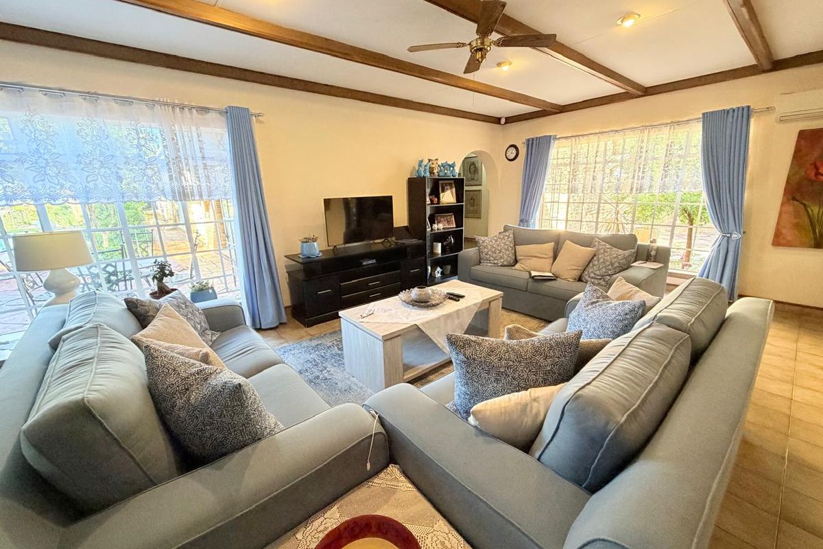 Spacious living room featuring exposed timber ceiling beams, tiled flooring, and large windows that provide ample natural light.