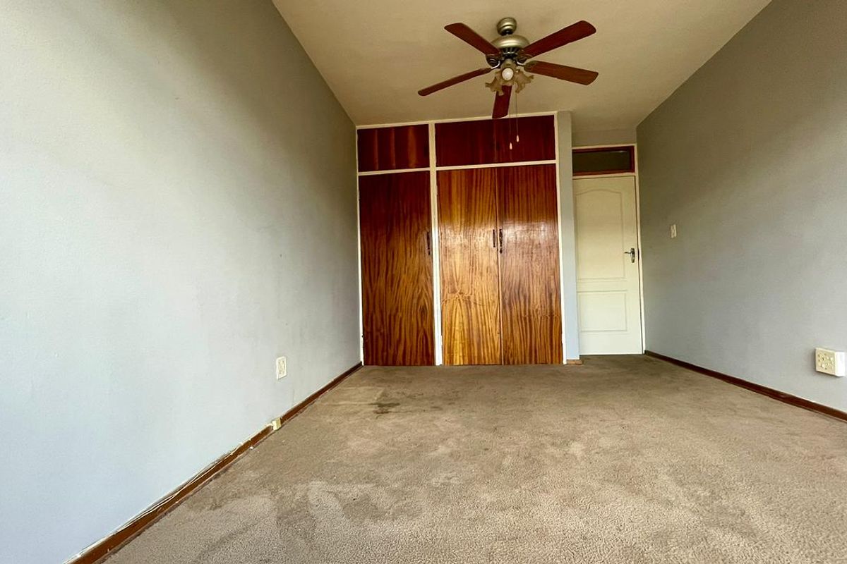 An empty bedroom featuring built-in wooden cupboards, a ceiling fan, and carpeted flooring, requiring cosmetic updates to improve its overall condition.