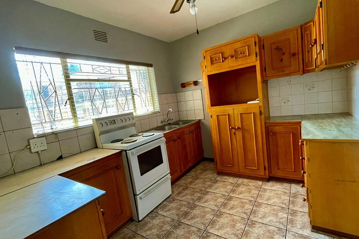 A functional kitchen featuring wooden cabinetry, tiled splashbacks, a freestanding stove, and tiled flooring, offering a classic layout with potential for modernization.
