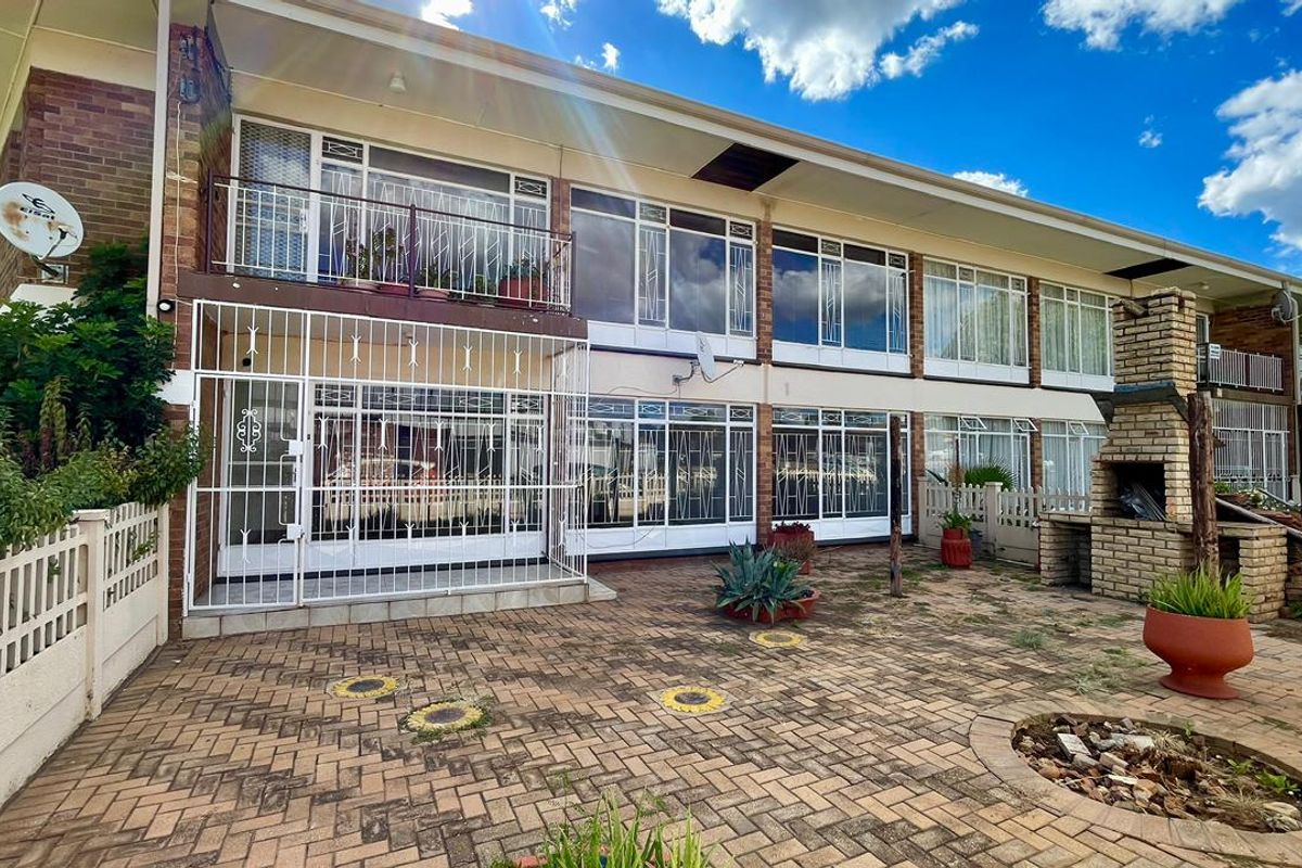 Rear exterior view of the apartment building featuring a paved courtyard, built-in brick braai, and balcony access with security gates.