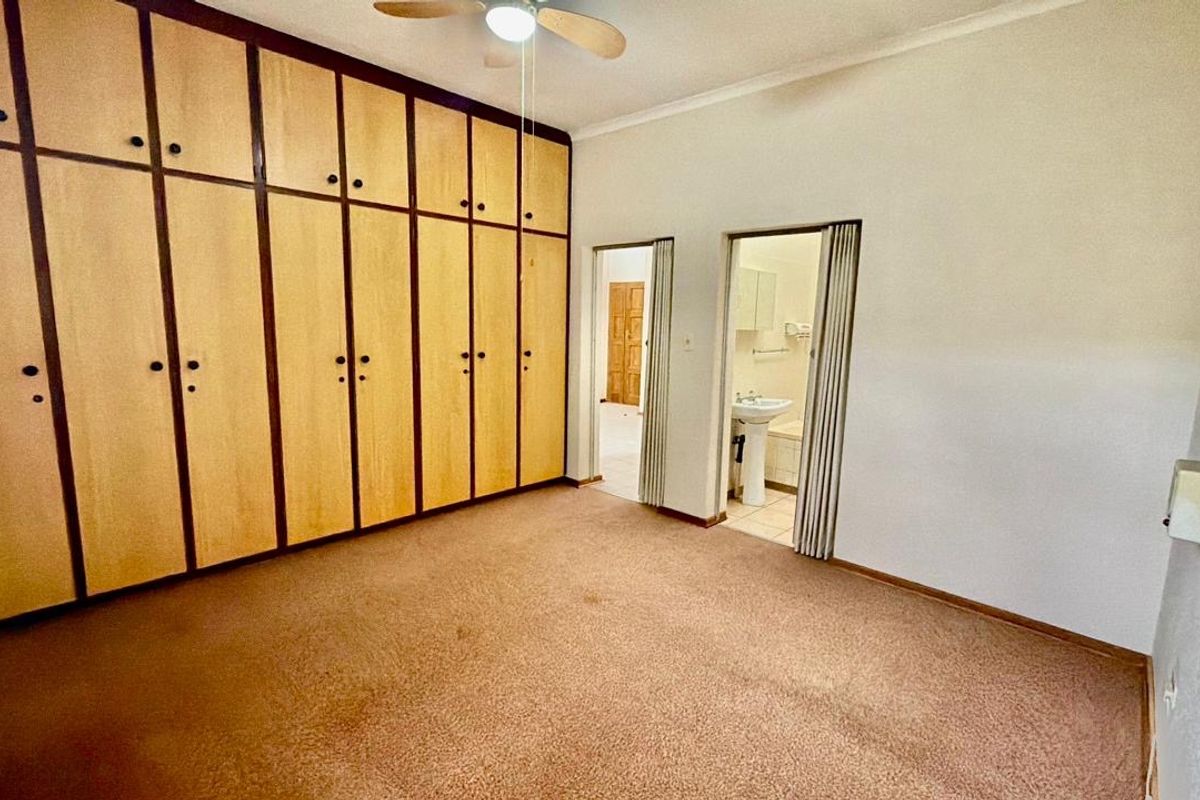 Spacious bedroom featuring extensive built-in cupboards, a ceiling fan, and direct access to an en-suite bathroom.