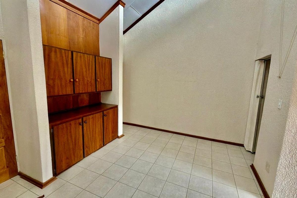 An empty living area featuring vaulted ceilings, tiled flooring, and integrated wooden cabinetry providing ample storage space.