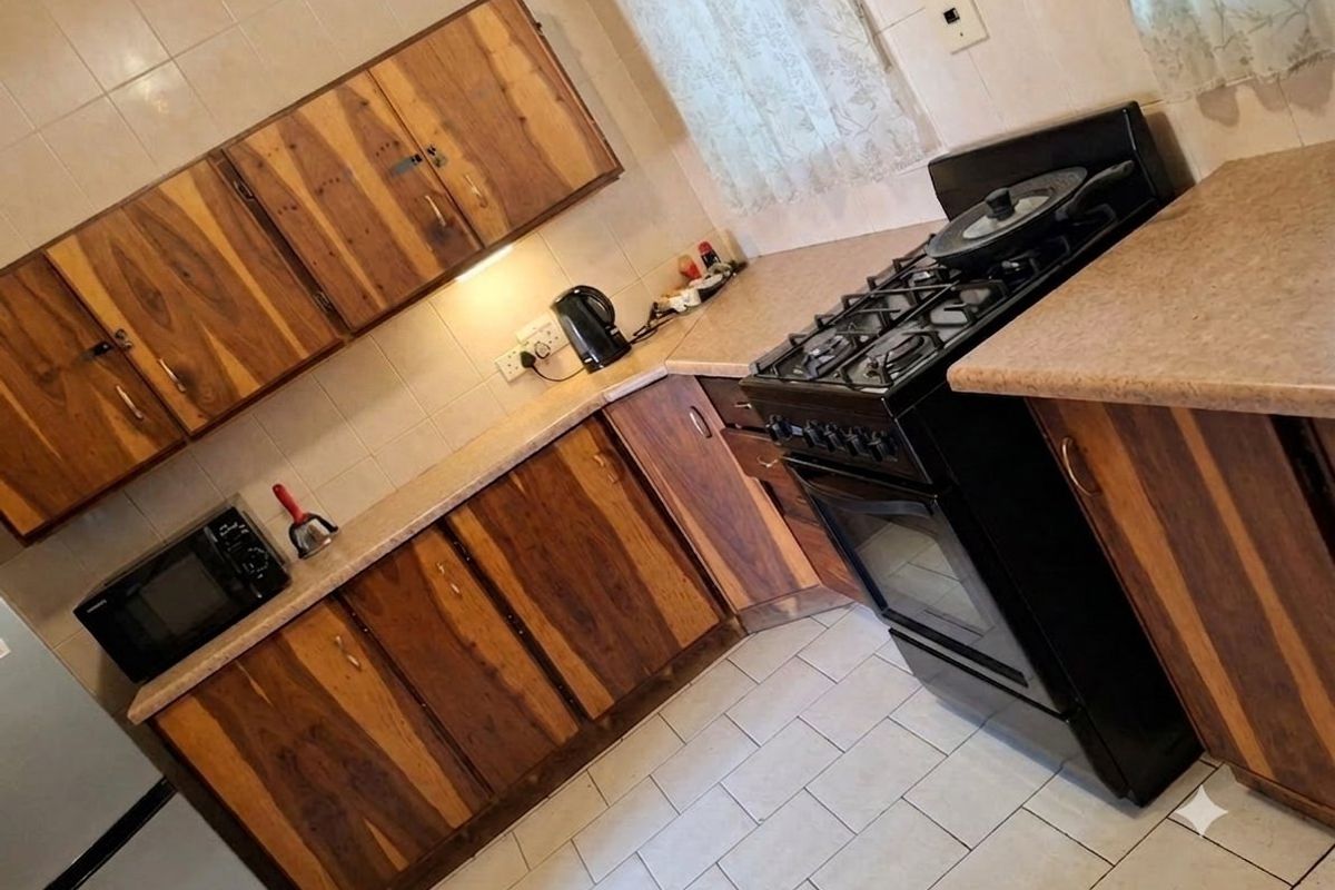 A functional kitchen featuring wooden cabinetry, laminate countertops, and a gas stove with tiled backsplash and flooring.